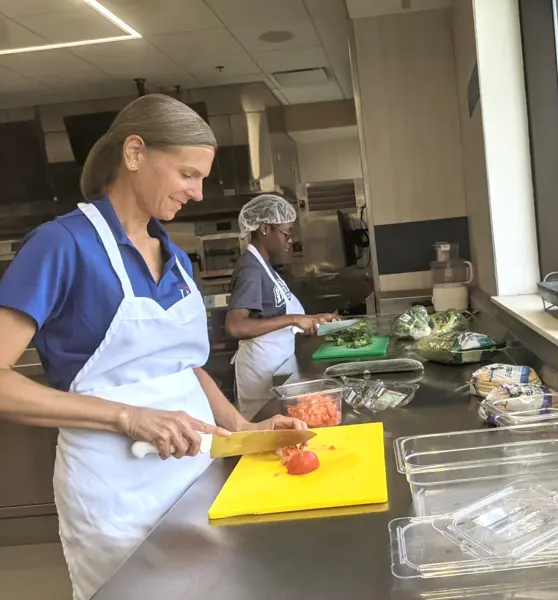 Two students wearing aprons and cutting vegetables in quantity food kitchen
