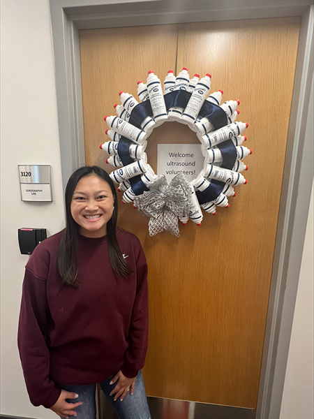 Student standing in front of a wreath made from ultrasound gel bottles