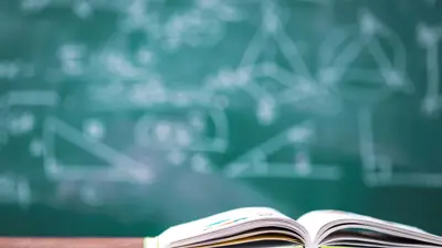 An open book on a desk in front of a chalkboard with math equations on it