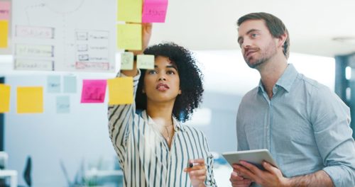 Two people work together by placing sticky notes on a board