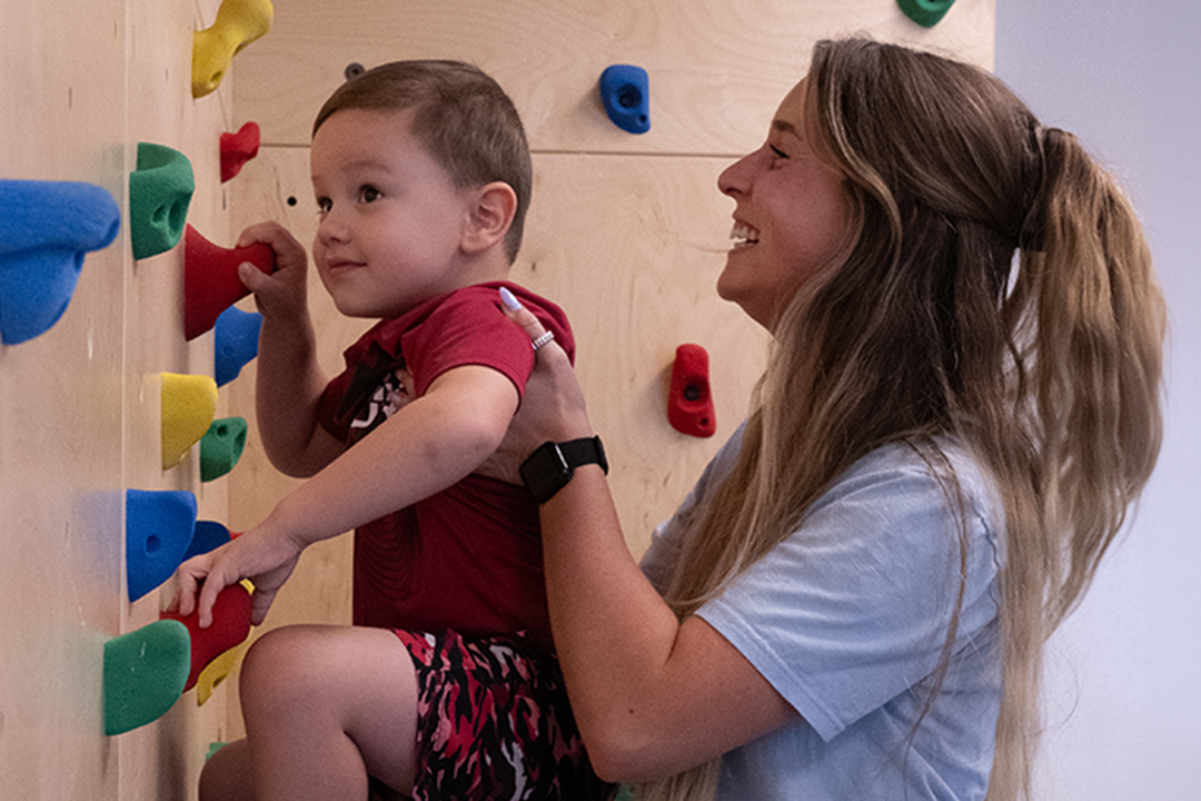 Student helping child use rock wall