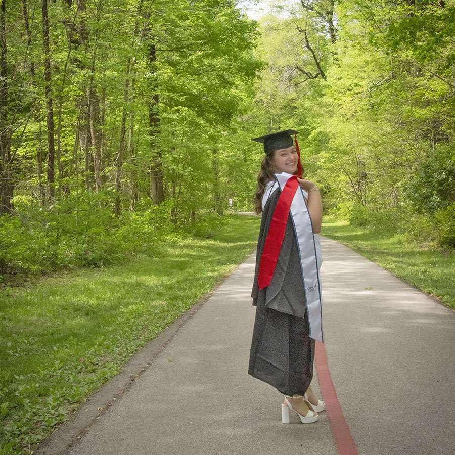 A 2025 graduate looks over her shoulder, her gown and honors stole thrown over her shoulder on USI's Bent Twig Trail 