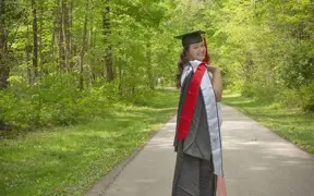 A 2025 graduate looks over her shoulder, her gown and honors stole thrown over her shoulder on USI's Bent Twig Trail 