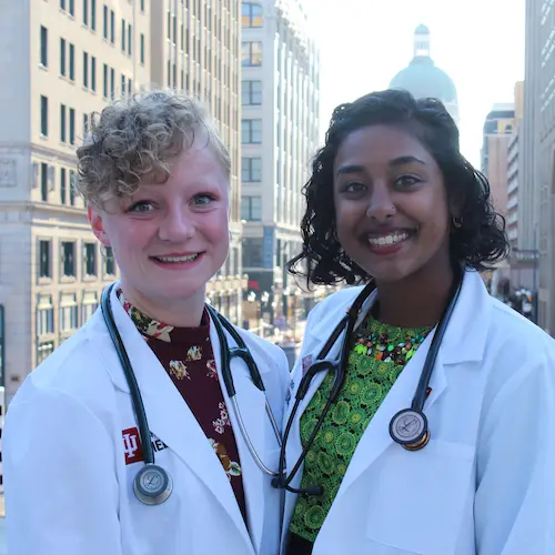 Two female pre-medical students pose for a photo in their white lab coats and stethescopes