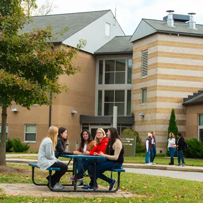 Students sitting at a picnic table in front of a residence hall.