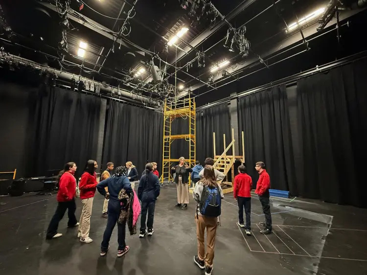 Students stand during rehearsal in the Mallette Studio Theatre, a black box theatre draped with black curtains