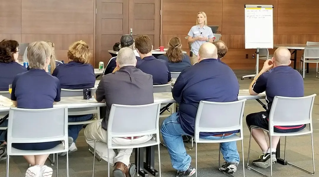Instructor teaches a group of adults in work uniforms in front of a flipchart