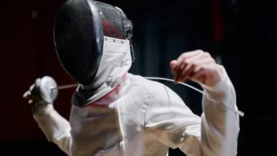 The individual is wearing a traditional white fencing jacket and a black mesh fencing mask with a white bib