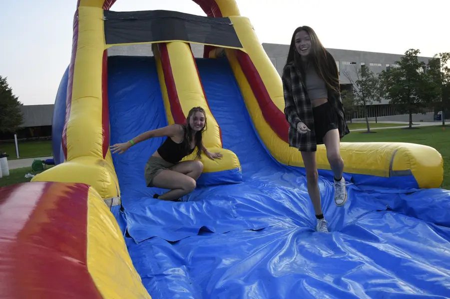 Students smile while sliding down an inflatable slide on the campus Quad