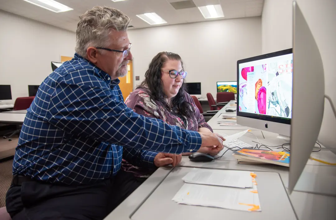 English faculty member works with a student in a computer lab