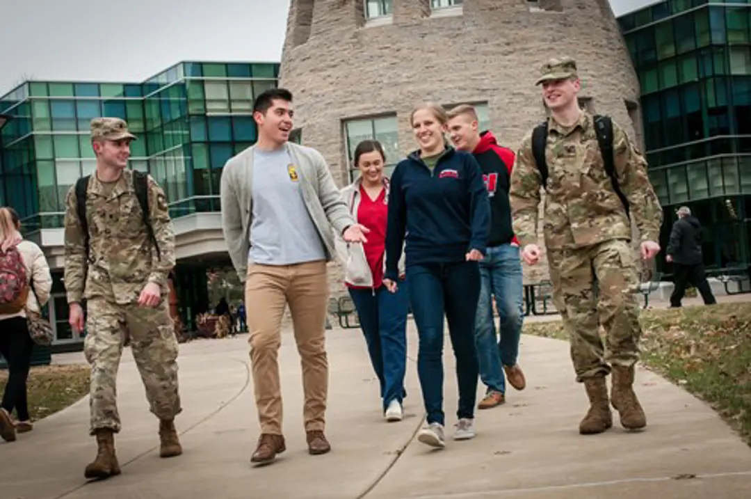 A group of students walk in front of the University Center, some of them in street clothes and some of them in military uniform