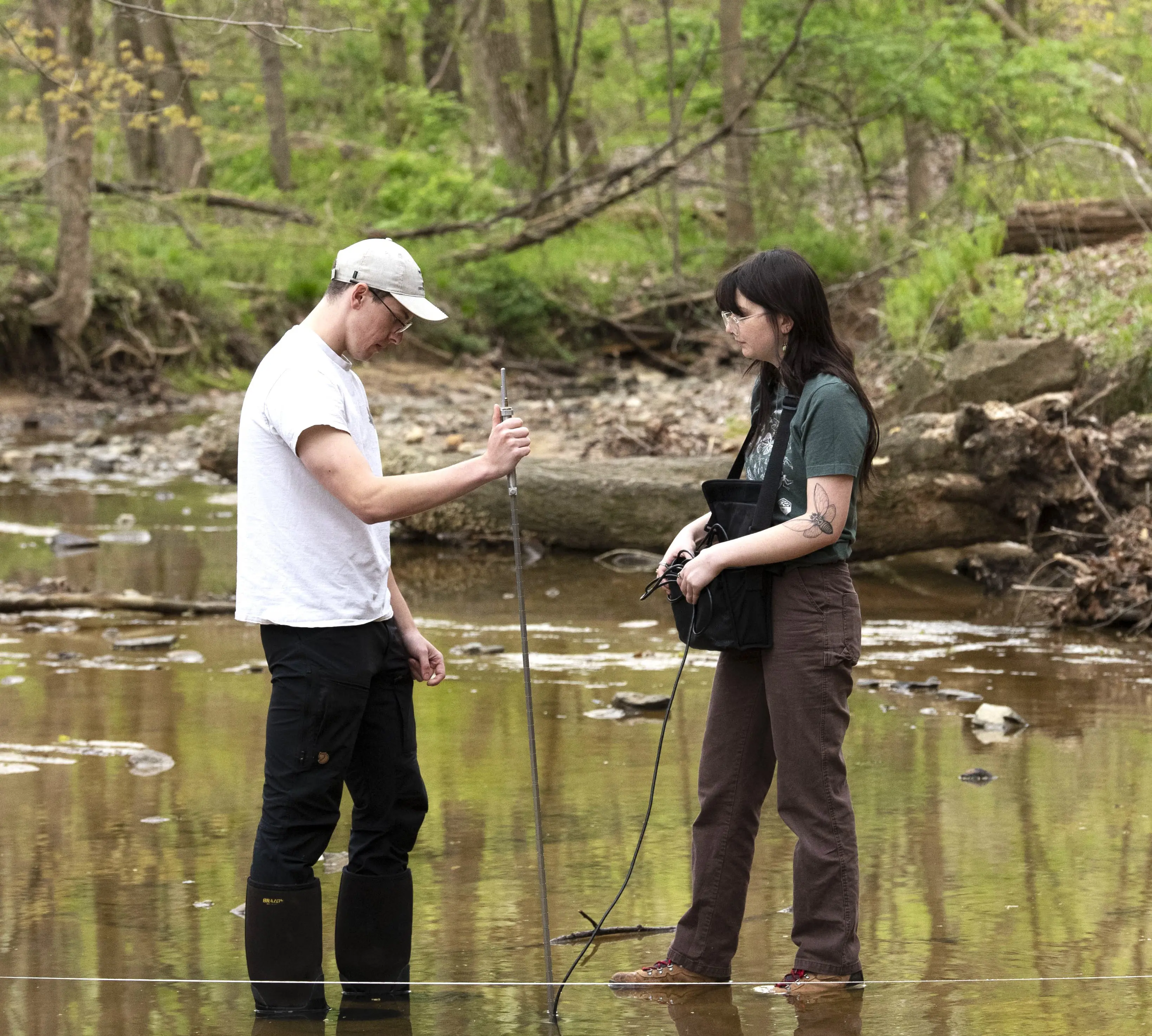 Geology students stand in a shallow creek with measuring devices