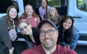 Students and faculty pose for selfie in front of a van