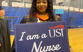 Master of Science in Nursing student in cap and gown holding "I am a USI Nurse" sign