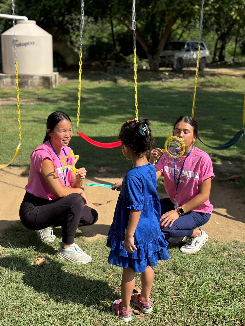 OT students blowing bubbles with child next to swingset