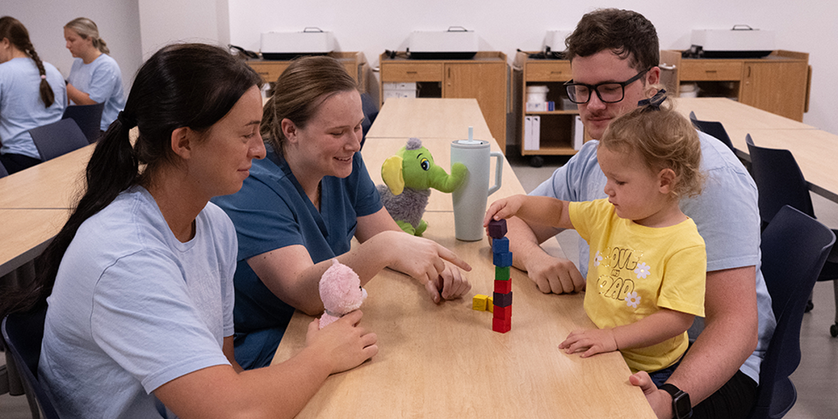 OT students helping child stack blocks