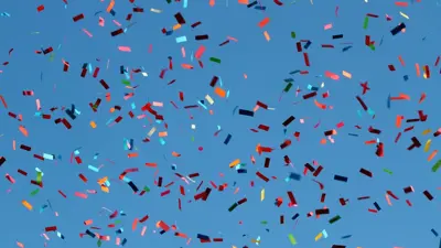 Multicolored paper confetti falls from a blue sky