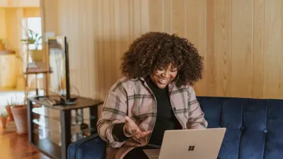 A smiling female student works on her laptop in her living room