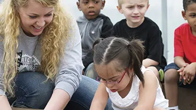 Student kneels down to work with children