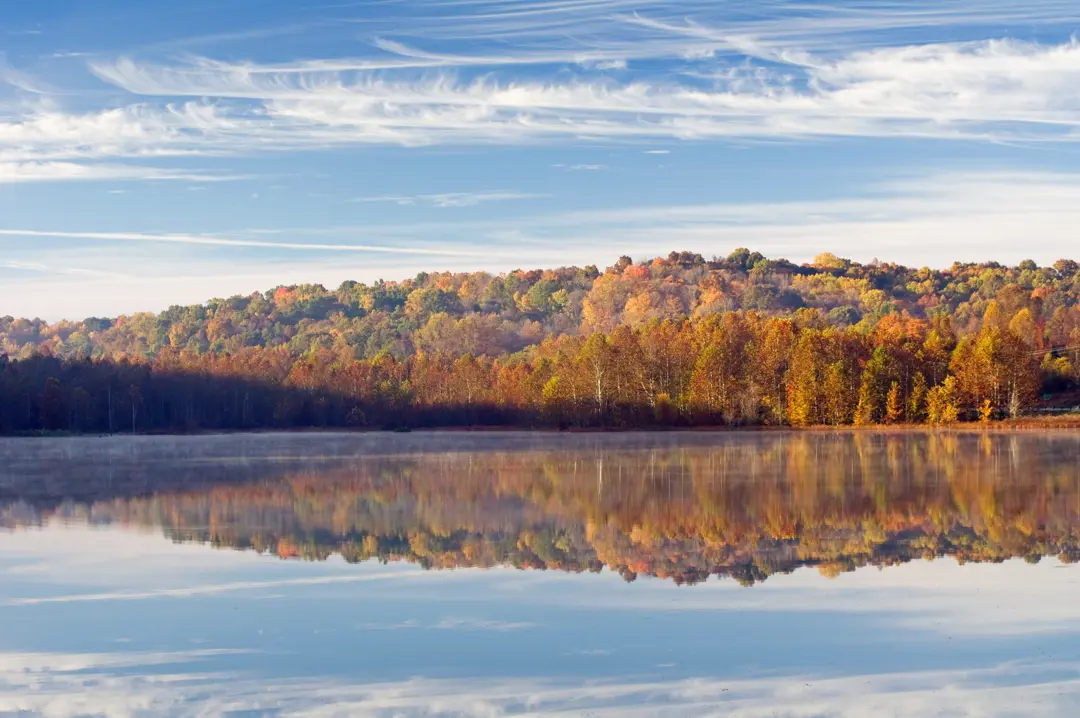 Patoka Lake on a windless fall day, with orange leaves on the trees visible in the reflection on the lake