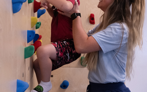 OT student helping child climb the rock wall
