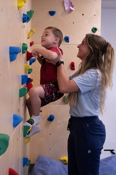 OT student helping child climb the rock wall
