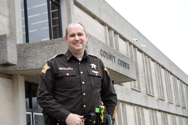 Casual portrait of USI sociology graduate Noah Robinson in his sheriff's department uniform standing in front of the Evansville Civic Center