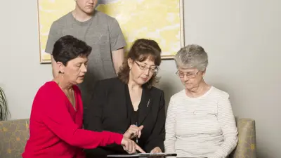 Nurse practitioner looking at medical chart with older adult, her daughter and grandson