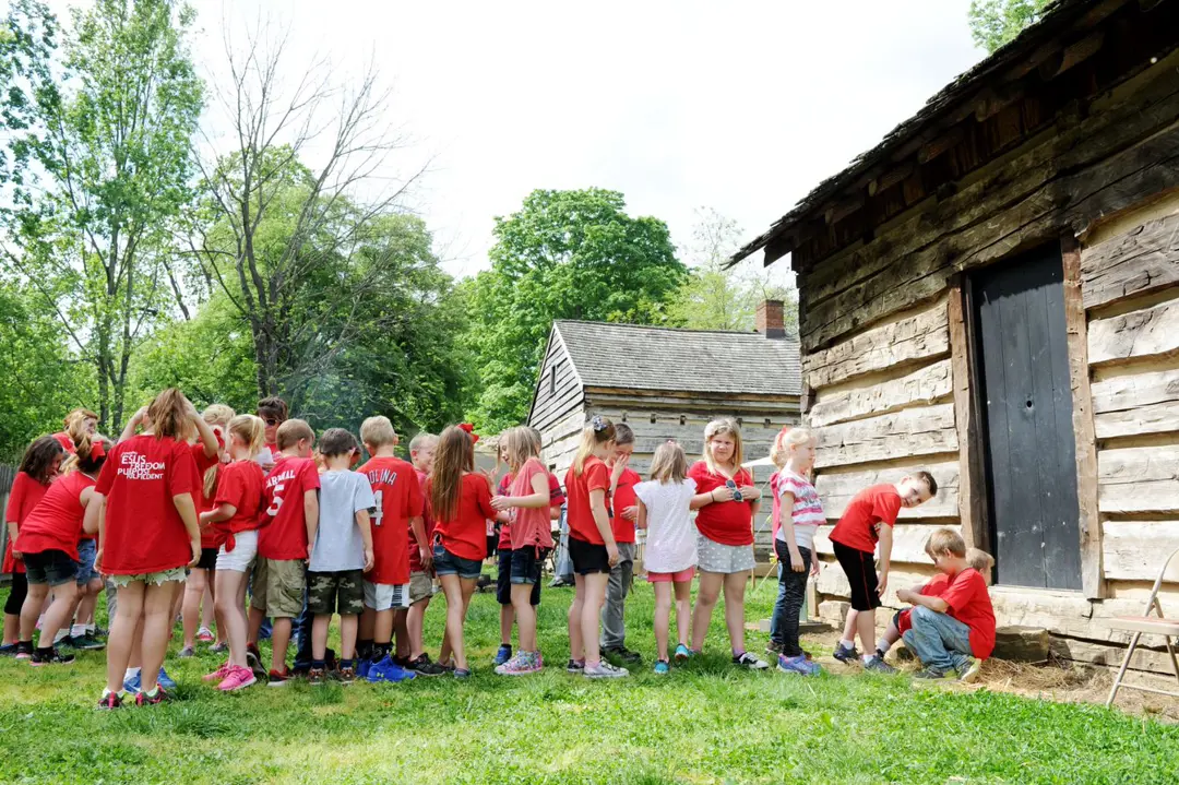 Children form a line in front of New Harmony's Weber Log Cabin