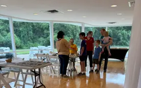 Group of people standing in a bright room with large windows overlooking greenery.