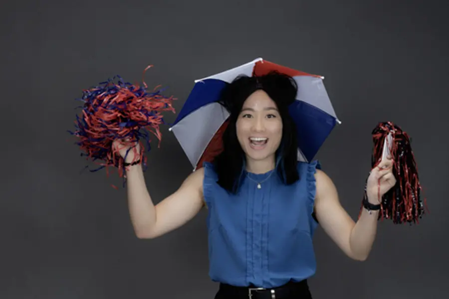 A member of the homecoming court, known for wearing an umbrella hat at new student orientation wears her umbrella hat and shakes pom poms.