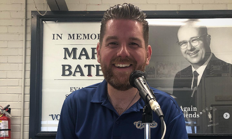 USI journalism graduate Zane Clodfelter smiles in front of a microphone wearing his Evansville Otters polo