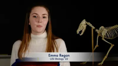 Video still of student Emma Regan with a preserved animal skeleton in the background