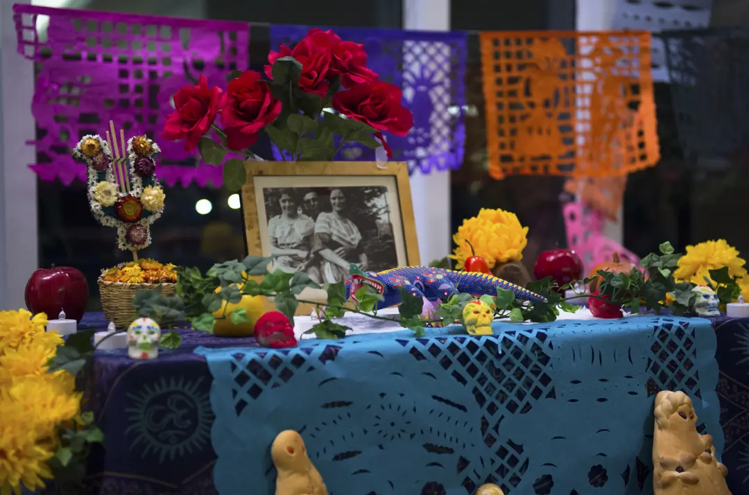 A colorful Mexican ofrenda, a table set with family photos, flowers, apples, and an alebrije
