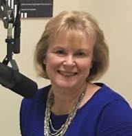 photo of Lauren Vicker is wearing a blue top and a necklace and is next to a microphone.