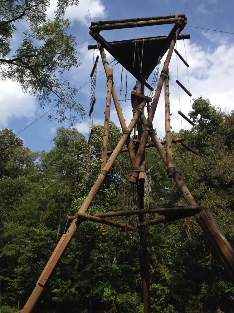 The image depicts the top of a climbing tower that uses ropes and harnesses to traverse.