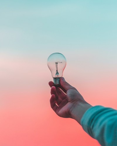 A person holds up a lightbulb in the sunset