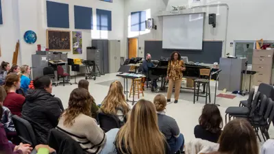 Vocal performance students listen to a woman perform accompanied by piano in the choir studio