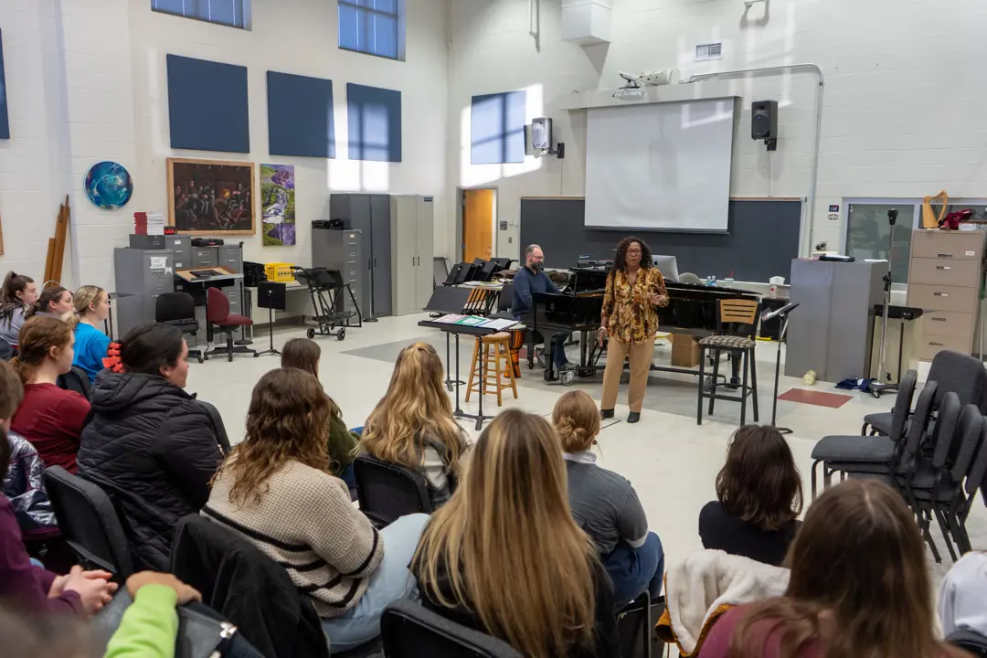 Vocal performance students listen to a woman perform accompanied by piano in the choir studio