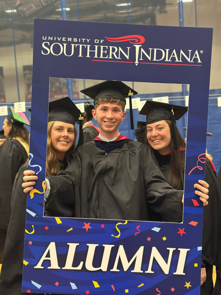 Three Occupational Therapy students wearing caps and gowns holding an alumni photo prop frame