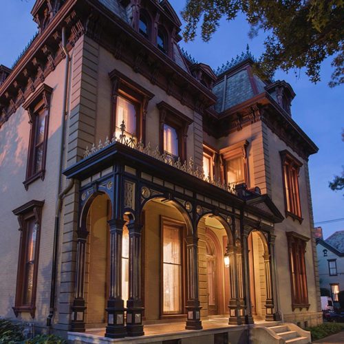 An old-fashioned two-story Victorian home with porch lights on.