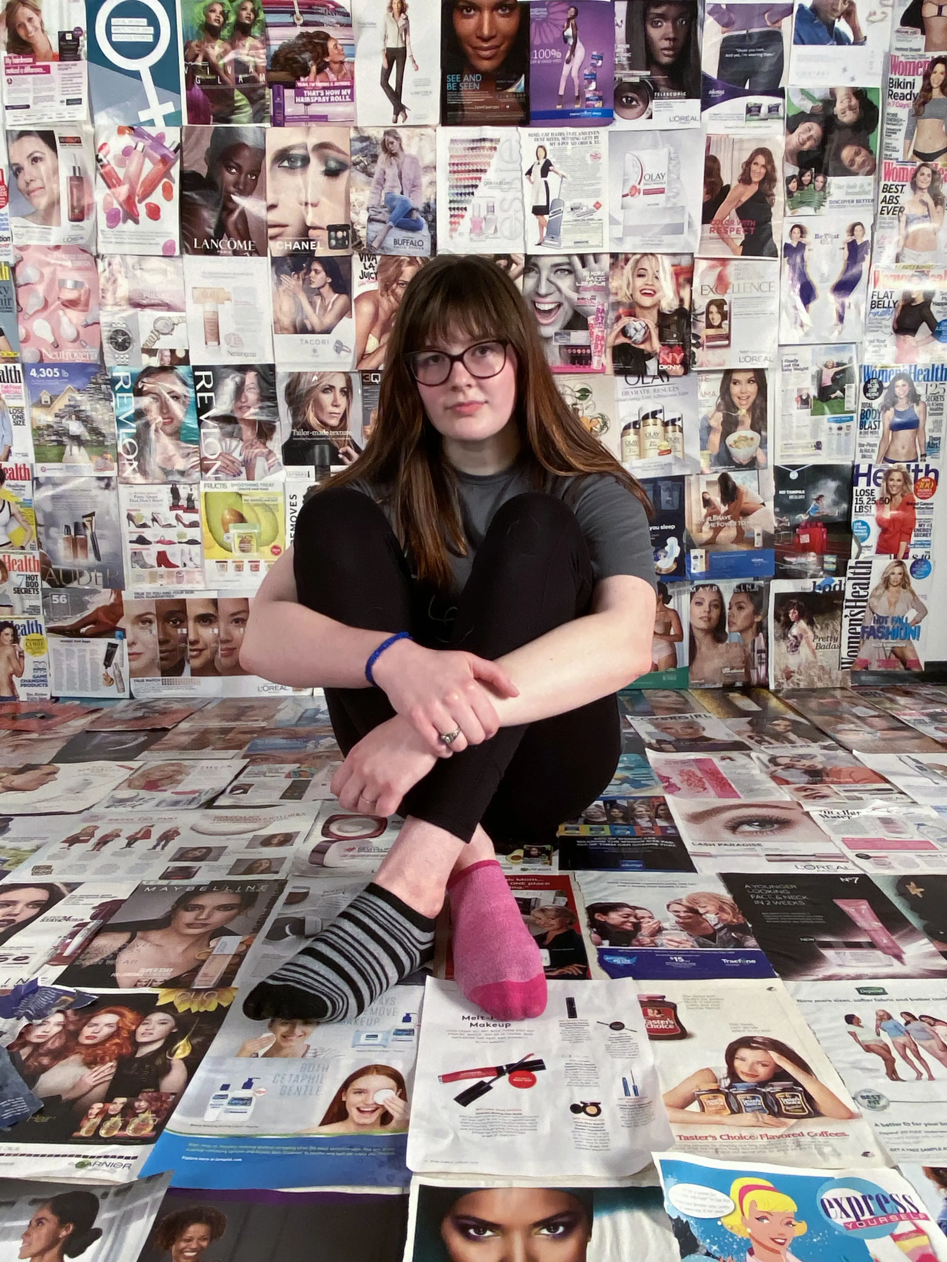 Photo of woman sitting on the floor in a room covered with fashion images.
