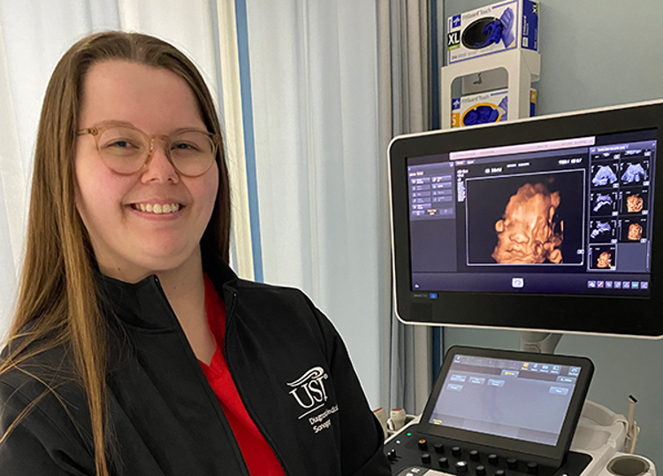 USI diagnostic medical sonography student Sarah McSparin poses in front of an ultrasound screen with an unborn baby on it