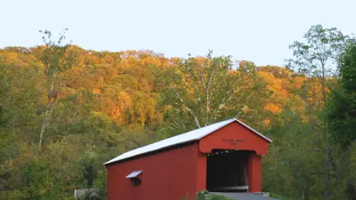 A view of the red Busching covered bridge with fall colored trees in the background