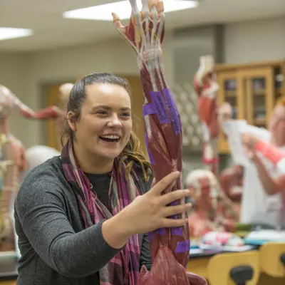 Student smiles while she practices touching a model arm with musculature