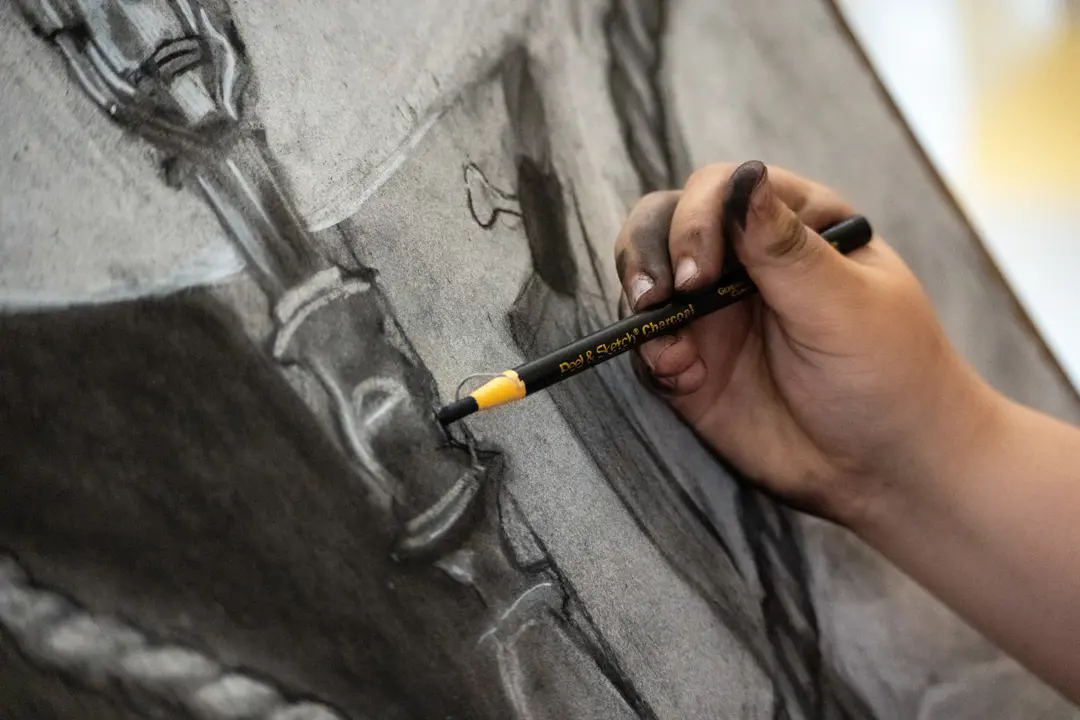 Close up of a student drawing with a black oil pencil