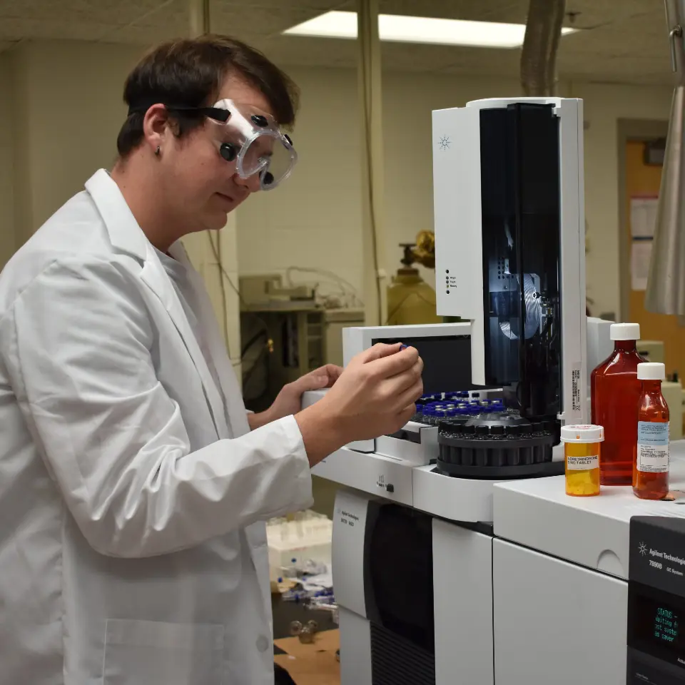 USI pre-pharmacy student in a lab coat and safety goggles working with a centrifuge machine