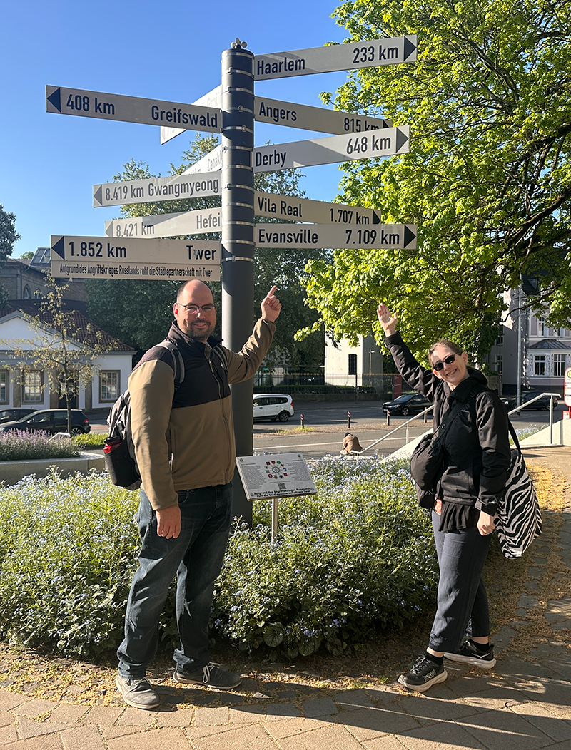 Photo of two faculty members in Germany standing in front of a sign with directions to other cities